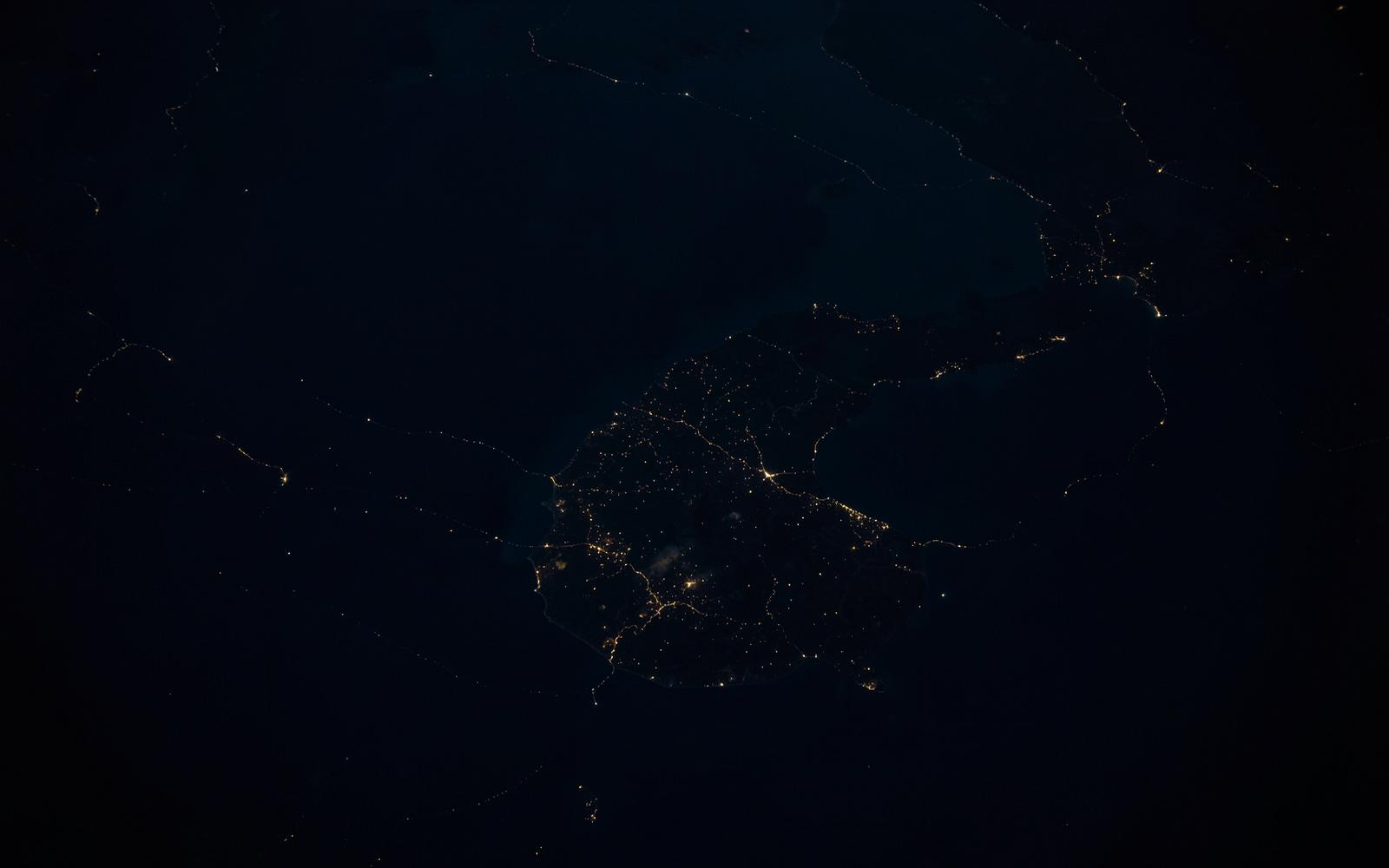 Aerial night view of a coastline and continental landmass with faint light traces
