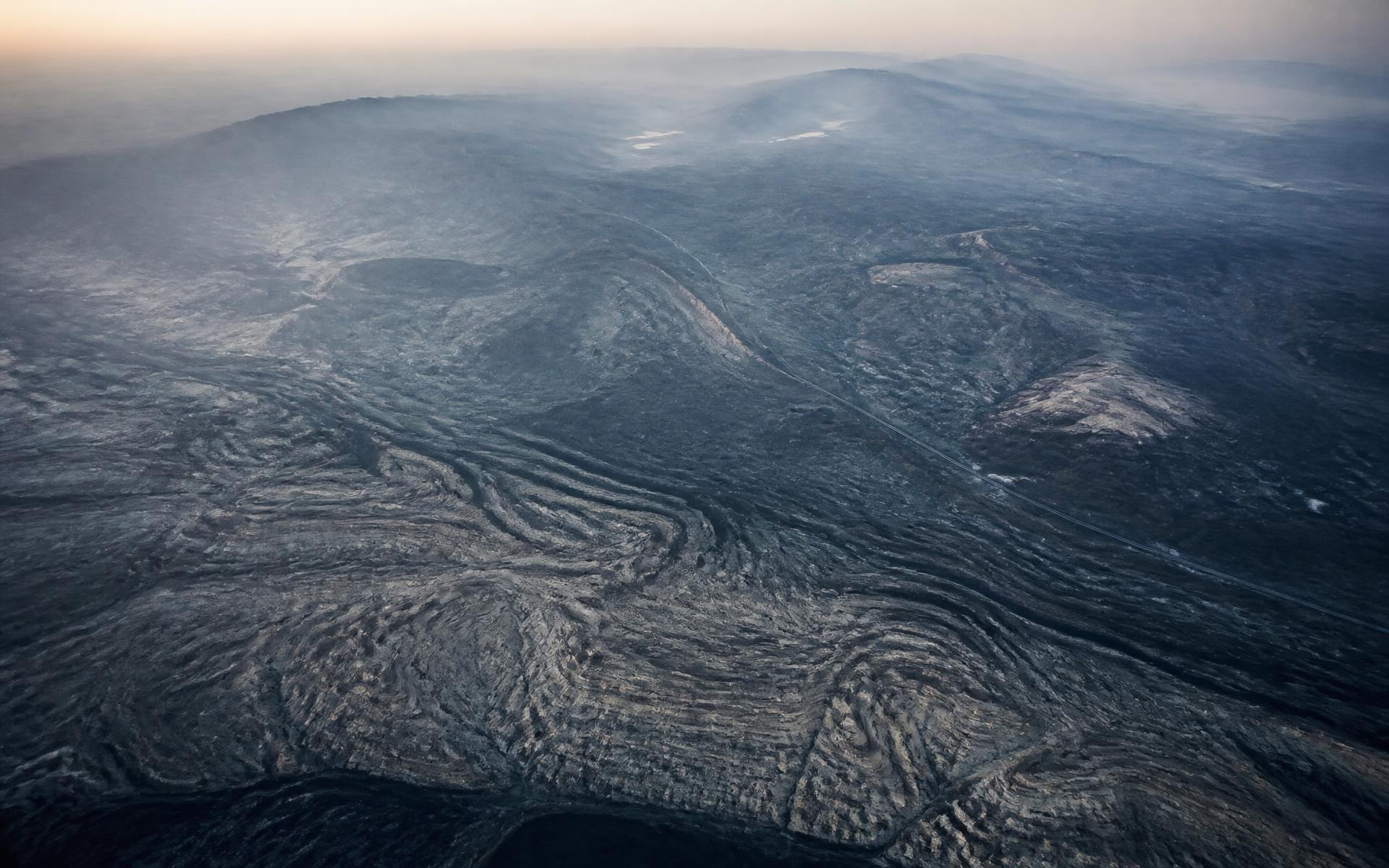 Aerial view of layered geological terrain crossed by a distant infrastructure corridor